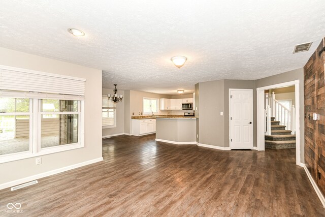 unfurnished living room with visible vents, an inviting chandelier, and dark wood-style floors
