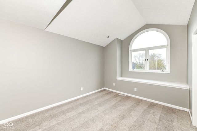 empty room with visible vents, baseboards, a textured ceiling, carpet flooring, and lofted ceiling