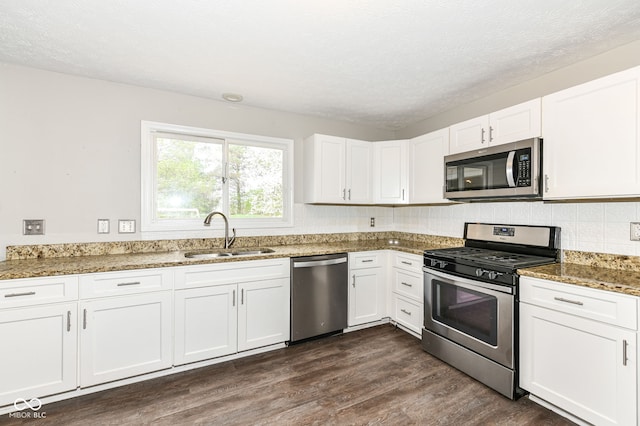 kitchen featuring dark wood finished floors, white cabinets, stone countertops, appliances with stainless steel finishes, and a sink