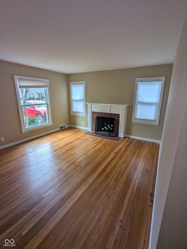 unfurnished living room with baseboards, visible vents, hardwood / wood-style flooring, and a fireplace