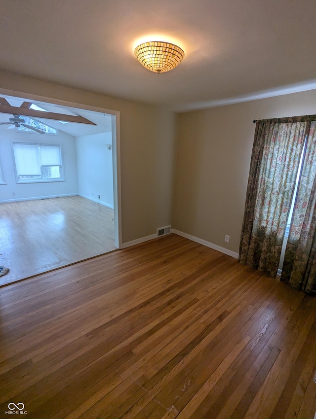 spare room featuring visible vents, a skylight, hardwood / wood-style flooring, baseboards, and a ceiling fan