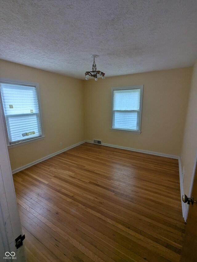 unfurnished room with wood-type flooring, baseboards, a chandelier, a textured ceiling, and visible vents