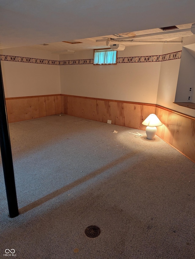 carpeted spare room with wooden walls and wainscoting