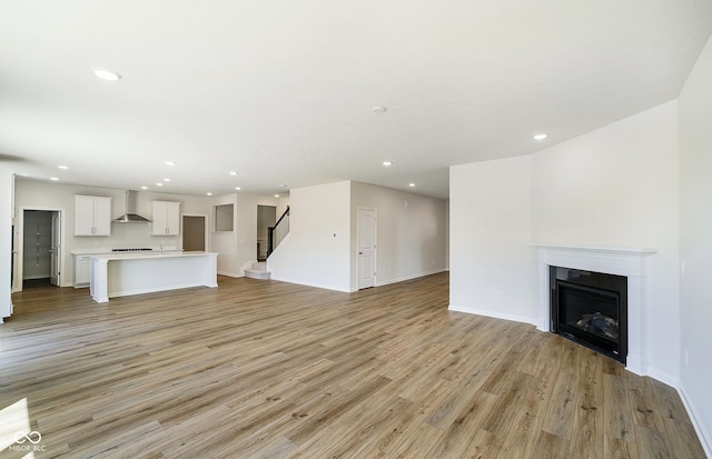 3241 Fawn Cir, Brownsburg, IN 46112 - unfurnished living room featuring light wood finished floors, recessed lighting, baseboards, a fireplace, and stairway