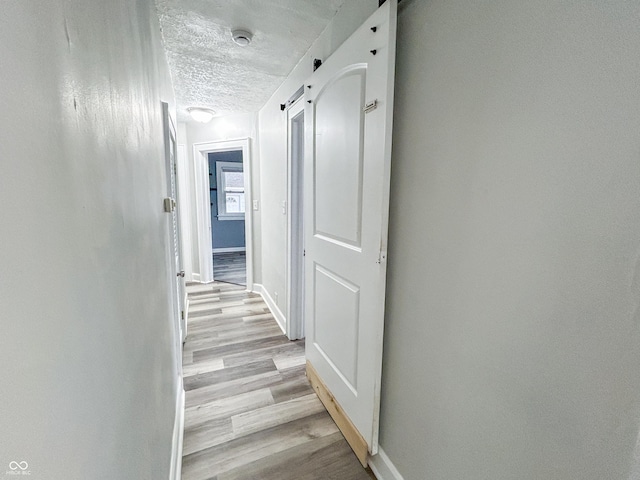 1627 E 8th St, Anderson, IN 46012 - hallway with a barn door, light wood-style flooring, a textured ceiling, and baseboards