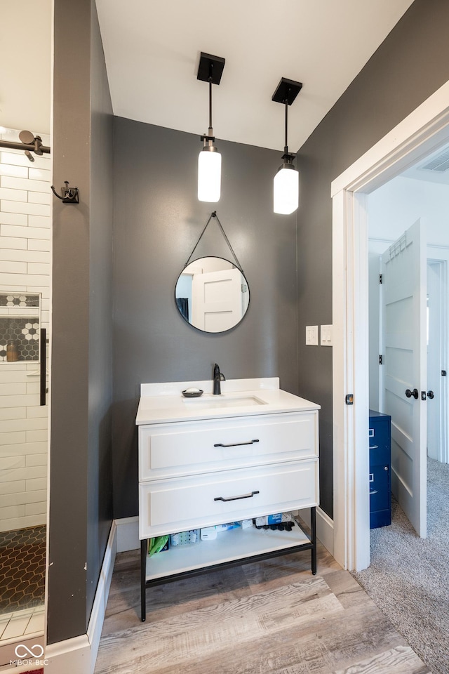 bathroom featuring vanity, baseboards, a tile shower, and wood finished floors