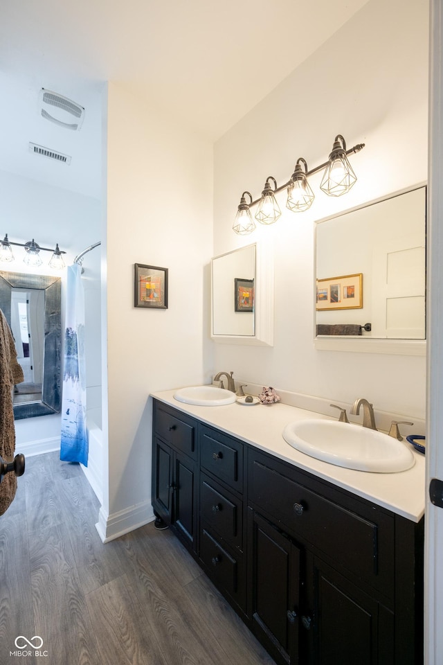 full bath with double vanity, visible vents, a sink, and wood finished floors