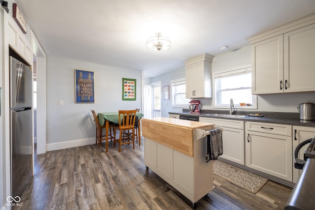 kitchen with a sink, dark wood finished floors, freestanding refrigerator, baseboards, and dishwashing machine