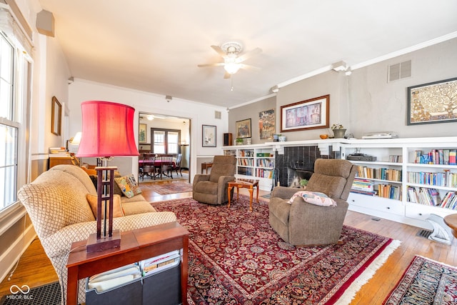 living area featuring a ceiling fan, visible vents, ornamental molding, and hardwood / wood-style floors