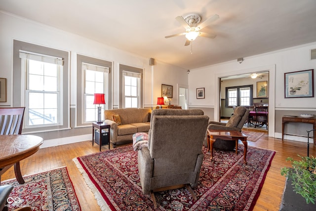 living room with ceiling fan, visible vents, light wood-type flooring, baseboards, and ornamental molding