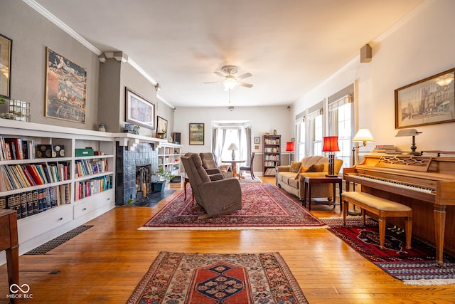 living area featuring ornamental molding, a ceiling fan, hardwood / wood-style flooring, and a tile fireplace