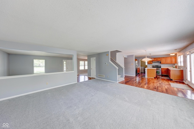 5989 Ashmore Ln, Carmel, IN 46033 - unfurnished living room featuring a textured ceiling, light colored carpet, stairway, healthy amount of natural light, and a sink