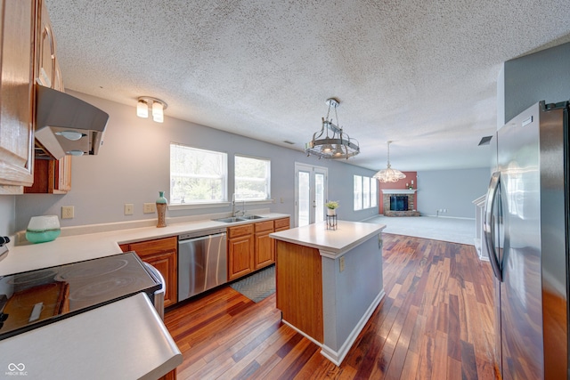 5989 Ashmore Ln, Carmel, IN 46033 - kitchen featuring appliances with stainless steel finishes, range hood, a kitchen island, light countertops, and a fireplace