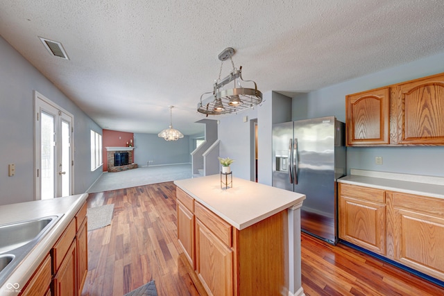 5989 Ashmore Ln, Carmel, IN 46033 - kitchen with stainless steel fridge with ice dispenser, a brick fireplace, light wood-style floors, a textured ceiling, and open floor plan
