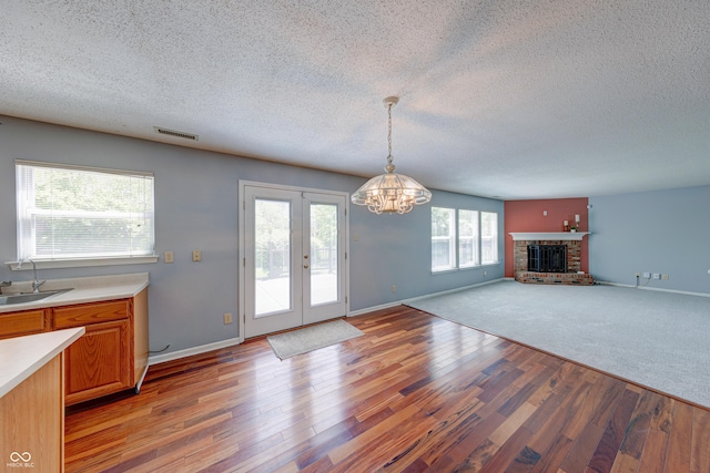 5989 Ashmore Ln, Carmel, IN 46033 - unfurnished living room featuring light wood-style flooring, a chandelier, a textured ceiling, a sink, and a brick fireplace