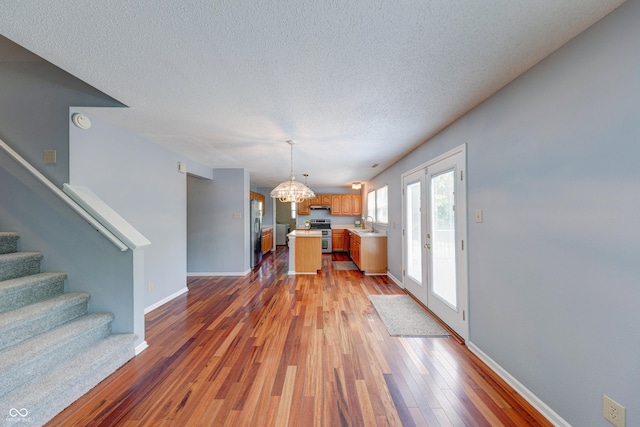 5989 Ashmore Ln, Carmel, IN 46033 - unfurnished living room featuring a chandelier, stairs, a textured ceiling, light wood-style floors, and baseboards