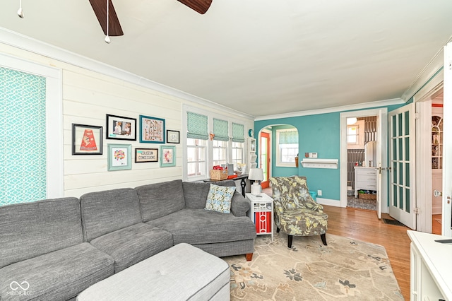 living area with a ceiling fan, arched walkways, wood finished floors, baseboards, and ornamental molding