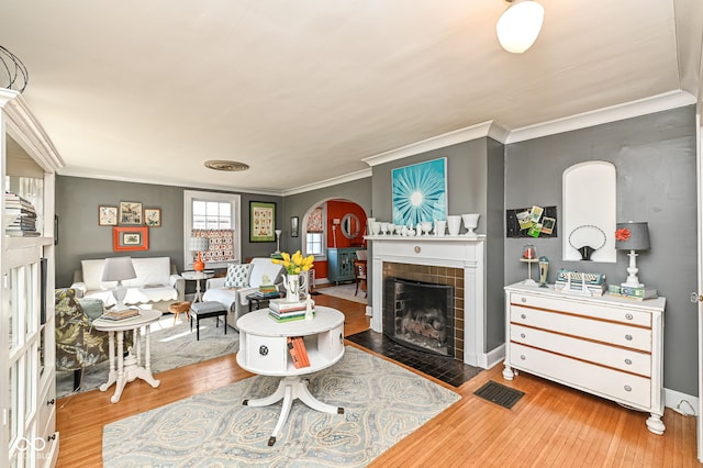 living room featuring a tiled fireplace, ornamental molding, arched walkways, and hardwood / wood-style floors