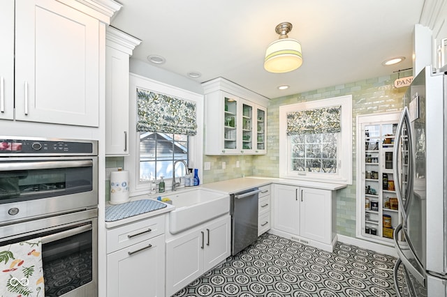kitchen with light countertops, white cabinets, a sink, backsplash, and stainless steel appliances