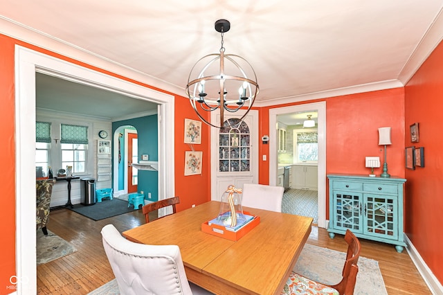 dining room with ornamental molding, baseboards, hardwood / wood-style flooring, arched walkways, and a notable chandelier