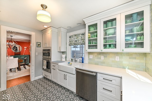 kitchen featuring appliances with stainless steel finishes, a sink, light countertops, a chandelier, and glass insert cabinets