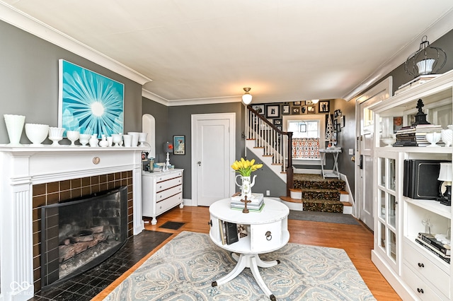 living area featuring ornamental molding, stairs, wood finished floors, and a tile fireplace
