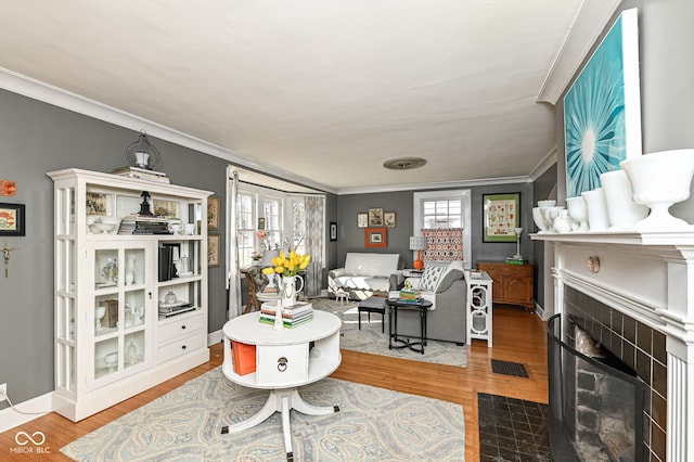 living area with ornamental molding, a tiled fireplace, and wood finished floors