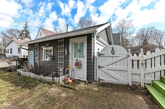 view of property exterior featuring a gate, fence, and a shingled roof