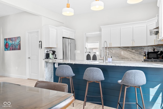 358 Terrace Ave, Indianapolis, IN 46225 - kitchen featuring washing machine and clothes dryer, decorative backsplash, high end refrigerator, light stone counters, and a kitchen breakfast bar