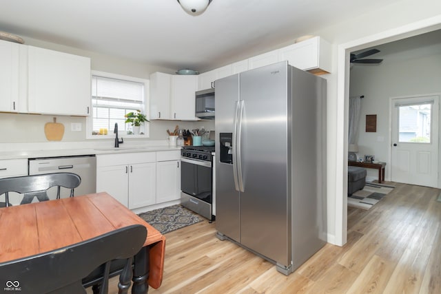 kitchen featuring light countertops, a sink, stainless steel appliances, white cabinets, and light wood-style floors