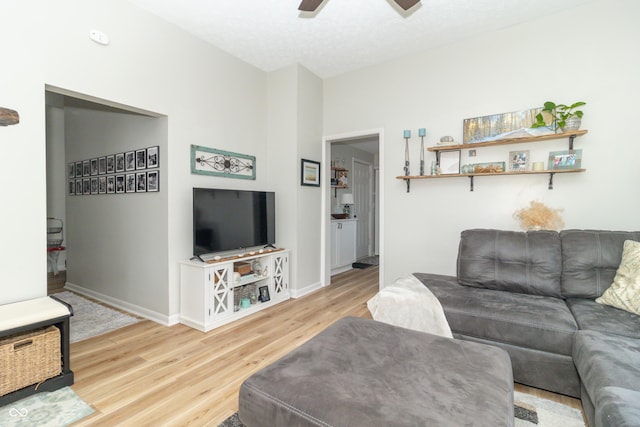 living area featuring a ceiling fan, light wood-style flooring, and baseboards