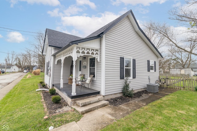 exterior space with covered porch, fence, a front lawn, a shingled roof, and central AC