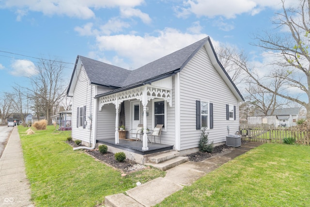 view of side of property with covered porch, roof with shingles, central air condition unit, fence, and a lawn