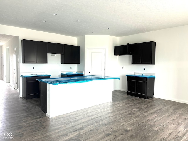kitchen with dark cabinetry, a textured ceiling, dark wood-style floors, and a center island