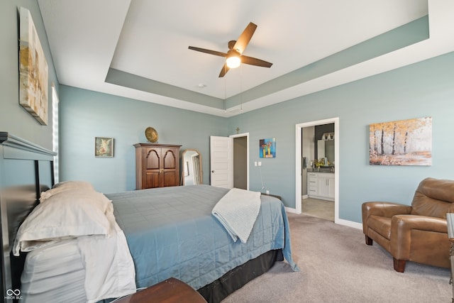 bedroom with carpet, baseboards, ceiling fan, ensuite bath, and a tray ceiling