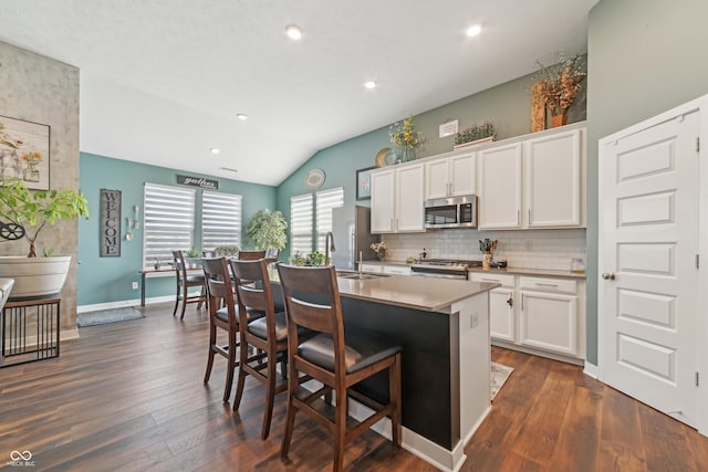 kitchen with stainless steel appliances, a breakfast bar area, lofted ceiling, and dark wood-type flooring