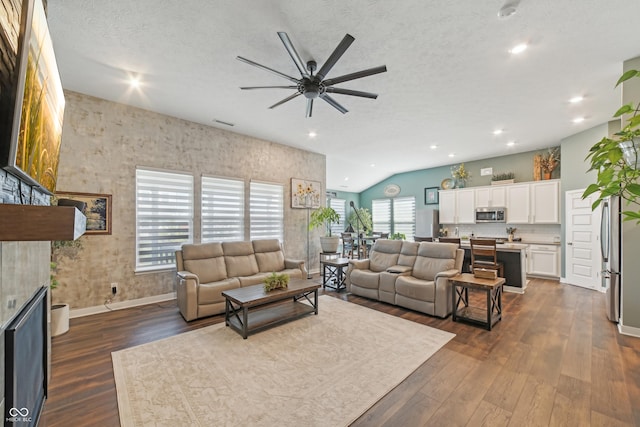 living area with a textured ceiling, baseboards, a ceiling fan, dark wood-type flooring, and vaulted ceiling