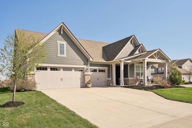 craftsman inspired home with stone siding, concrete driveway, a front yard, roof with shingles, and a porch