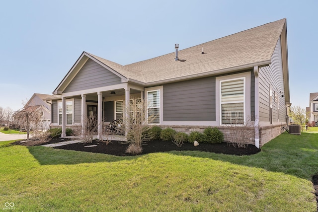 back of property with a porch, a shingled roof, central air condition unit, and a lawn