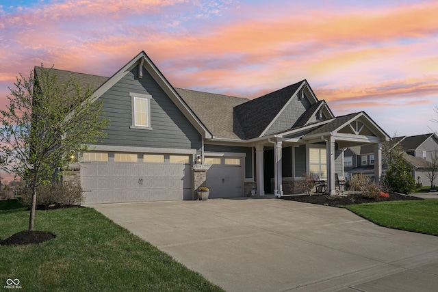 view of front of house with covered porch, concrete driveway, roof with shingles, an attached garage, and a yard