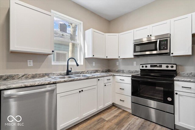 243 N Tacoma Ave, Indianapolis, IN 46201 - kitchen featuring appliances with stainless steel finishes, a sink, white cabinetry, light wood-style floors, and light countertops