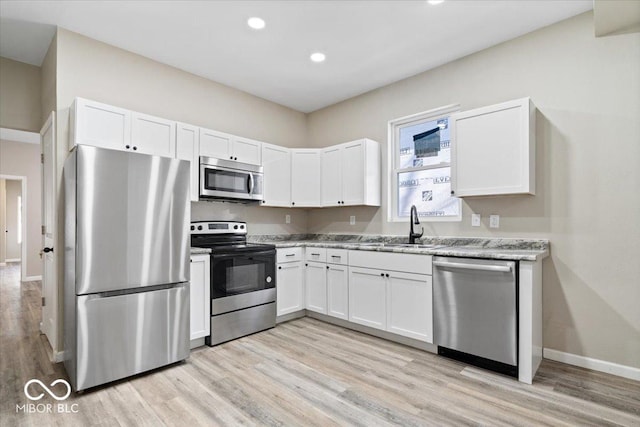 243 N Tacoma Ave, Indianapolis, IN 46201 - kitchen with stainless steel appliances, light wood-style floors, white cabinetry, a sink, and baseboards