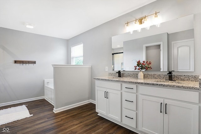bathroom with baseboards, double vanity, wood finished floors, and a garden tub