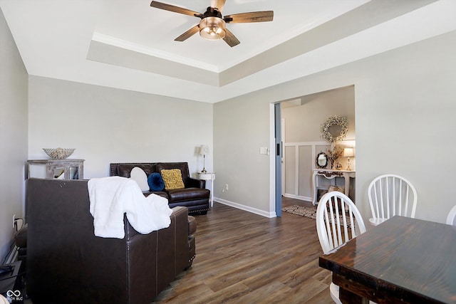 living room with a raised ceiling, dark wood-type flooring, baseboards, and ceiling fan
