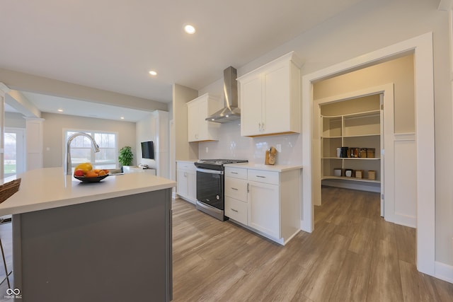 kitchen with gas range, light countertops, white cabinets, light wood finished floors, and wall chimney exhaust hood