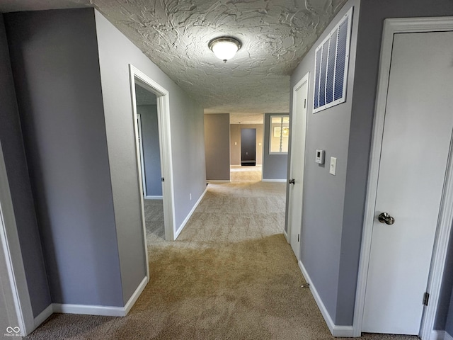 hallway with light carpet, baseboards, visible vents, and a textured ceiling