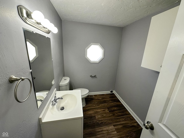 bathroom with vanity, toilet, baseboards, a textured ceiling, and wood finished floors