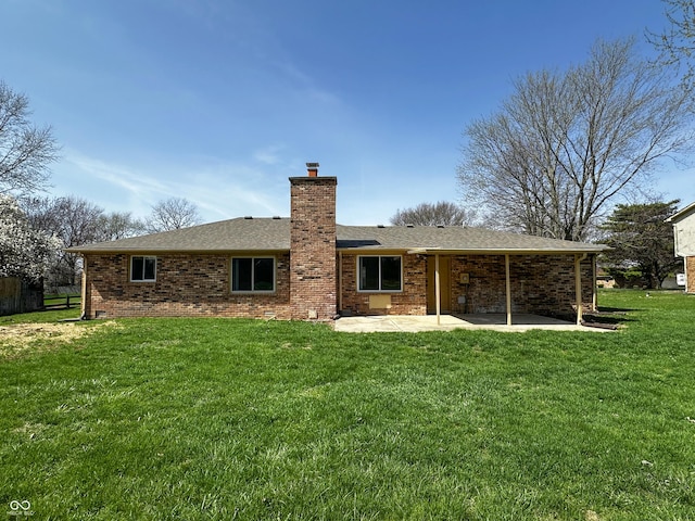 back of house featuring a patio area, roof with shingles, a chimney, brick siding, and a yard