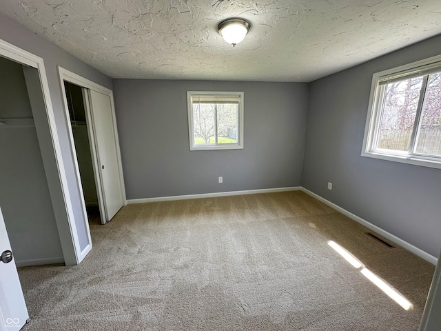 unfurnished bedroom featuring carpet floors, a textured ceiling, multiple closets, baseboards, and visible vents