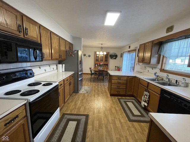 1310 Pin Oak Dr, Seymour, IN 47274 - kitchen with light wood-style flooring, a peninsula, a sink, black appliances, and an inviting chandelier